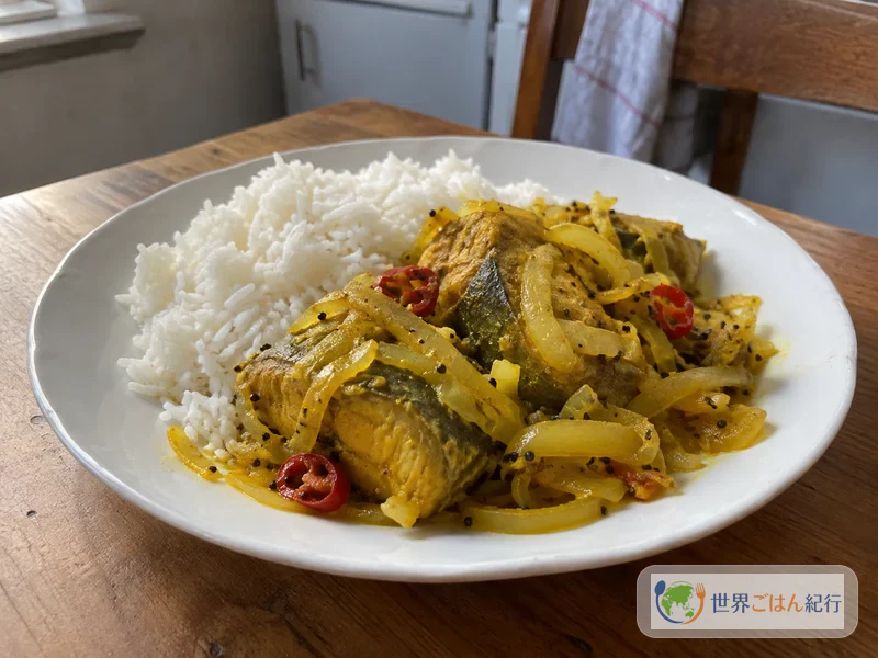 ご飯を盛った皿に、黄色いヴィンダイの魚と玉ねぎを添えたモーリシャスの家庭の昼ごはん