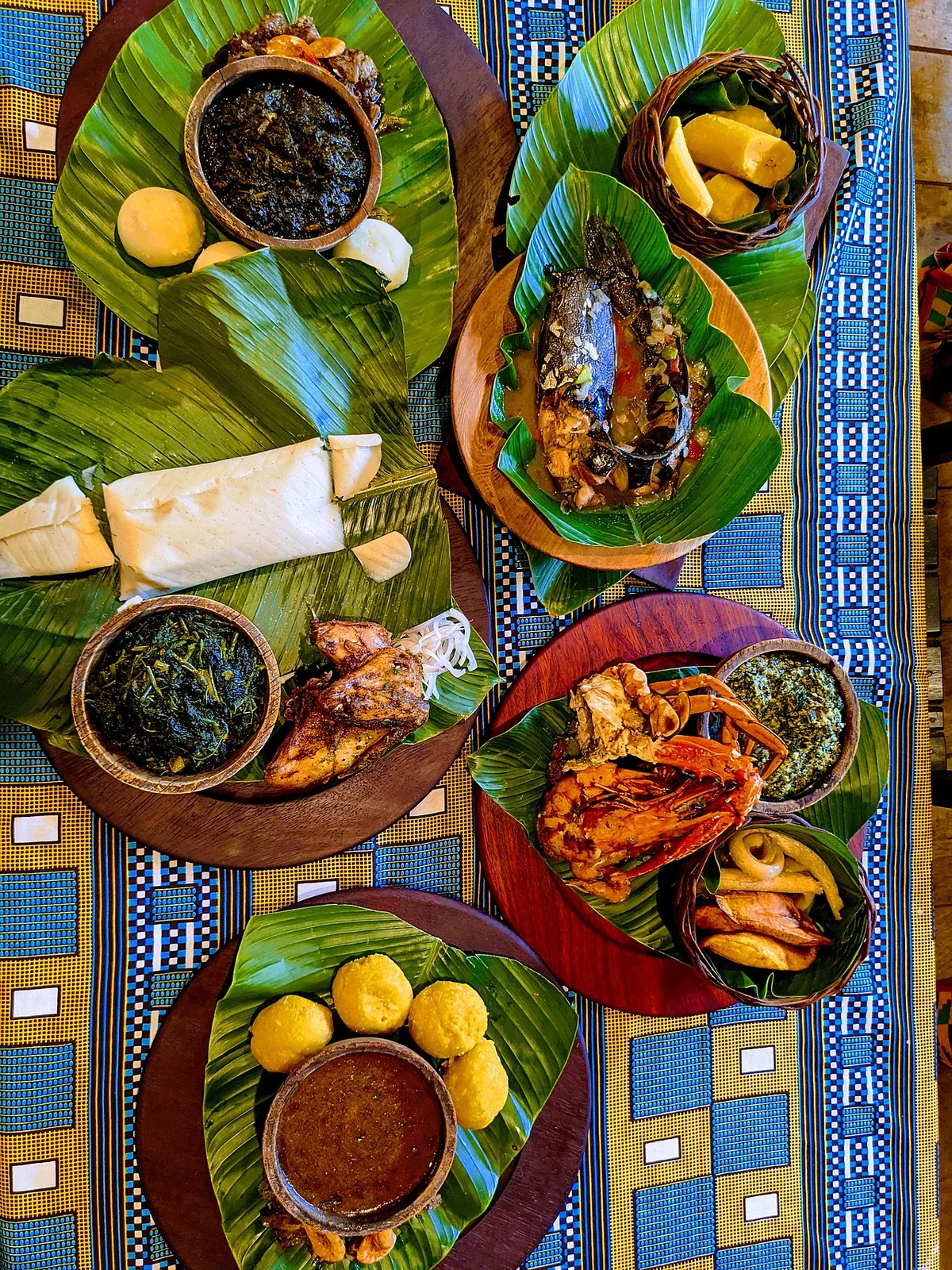 カメルーン料理の食卓。ンドレを含む複数の料理がバナナの葉の上に並んでいる
