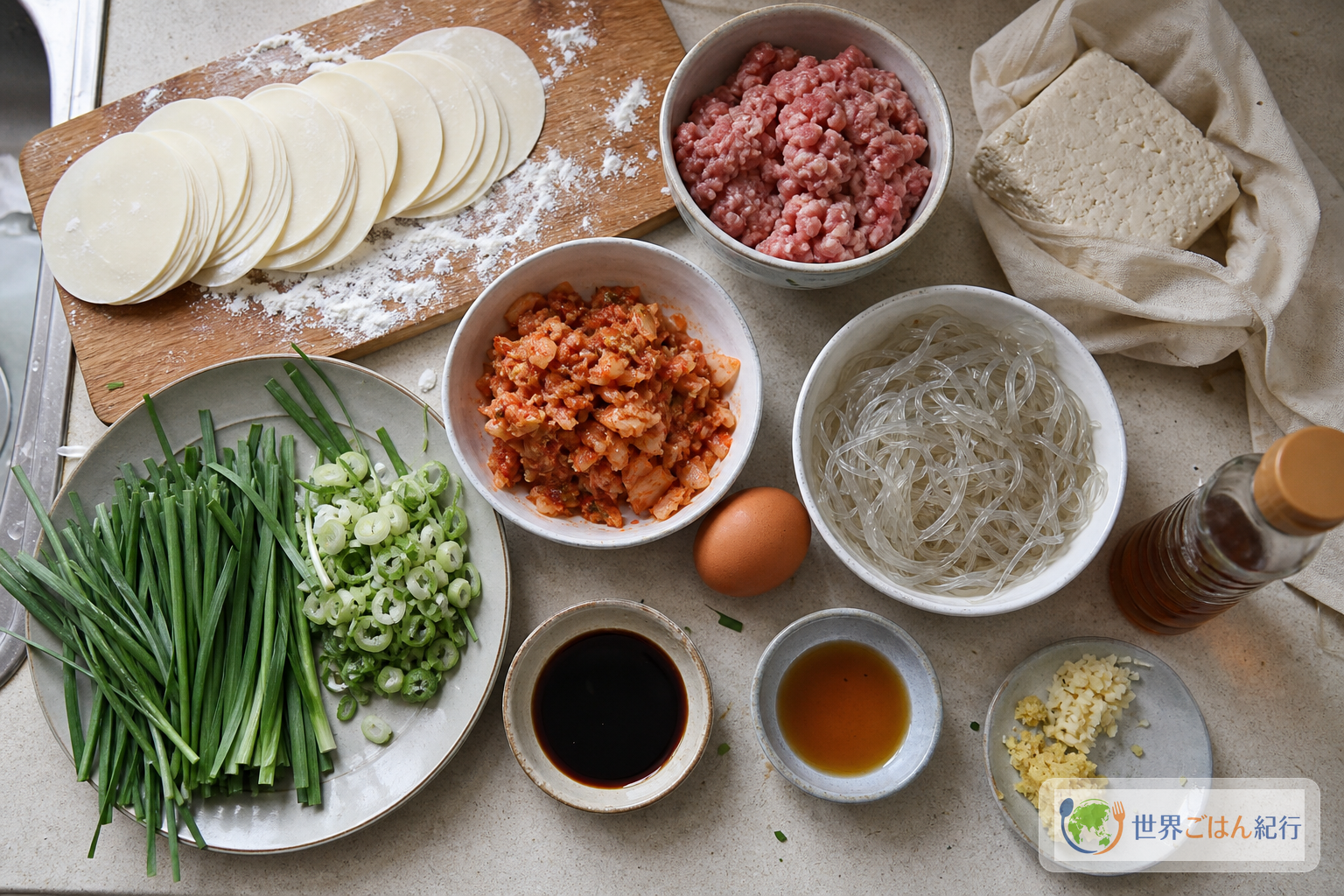 大判餃子の皮、豚ひき肉、木綿豆腐、キムチ、韓国春雨、にら、ねぎ、卵、しょうゆ、ごま油を並べたマンドゥの材料