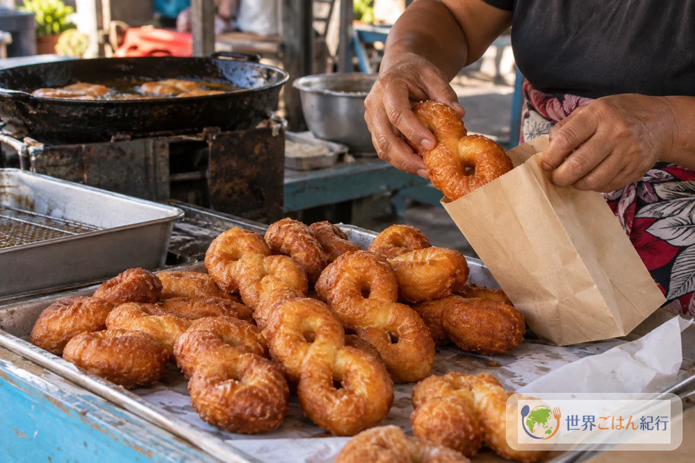 At a market stall in Tahiti early on a Sunday morning, figure-eight doughnuts being packed into paper bags for sale