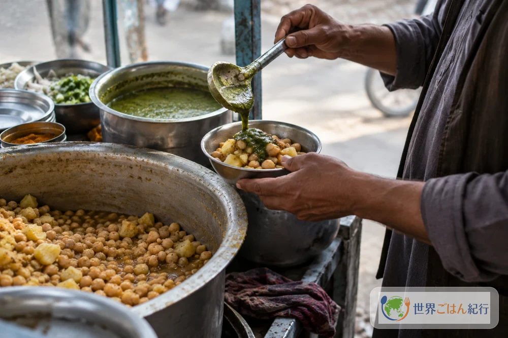 アフガニスタンの街角の屋台で、大鍋のひよこ豆とじゃがいもを椀によそい、緑のソースをかける売り手