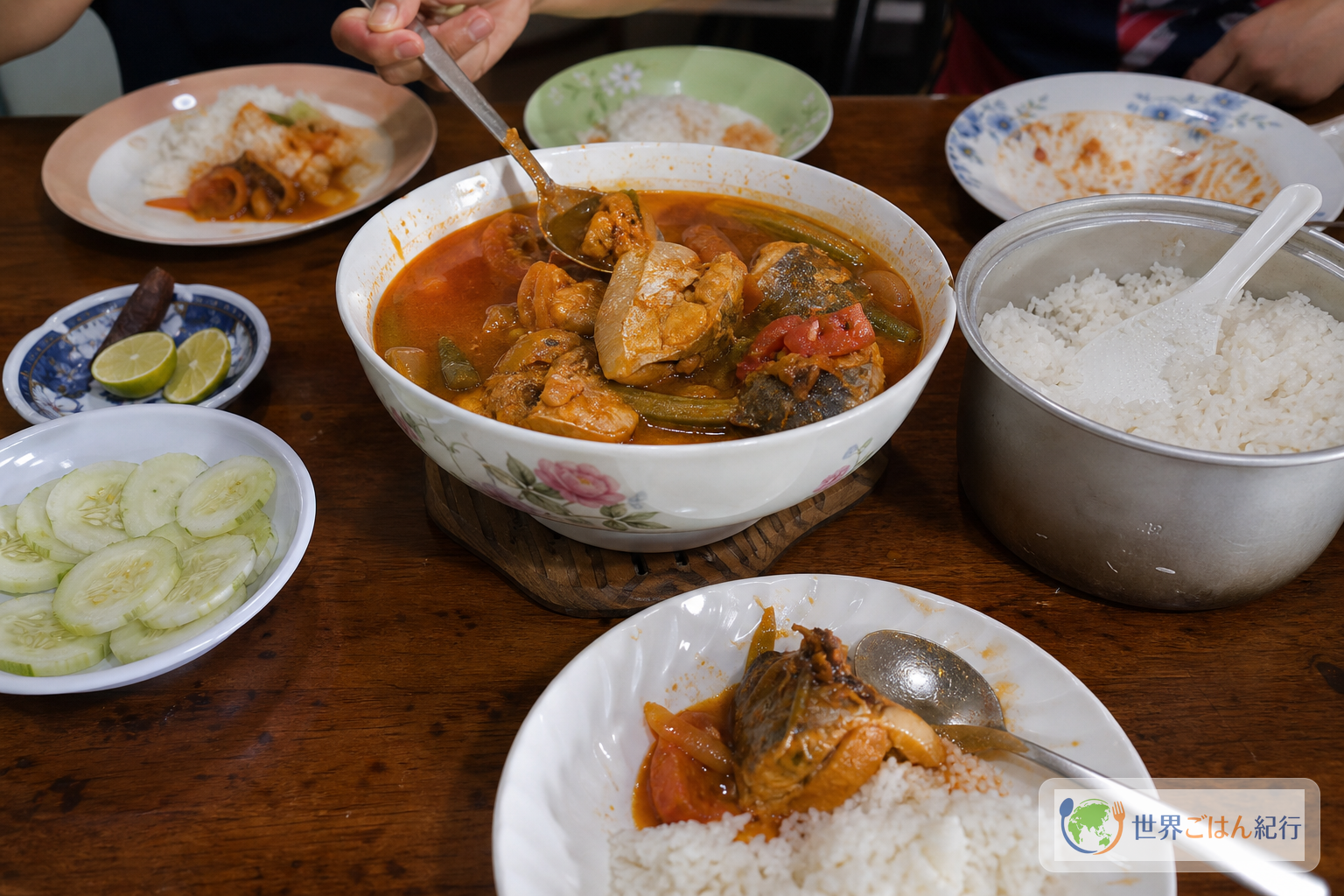 アッサムペダスを大皿で食卓に出し、ご飯、きゅうり、香草を添えた家庭の食卓