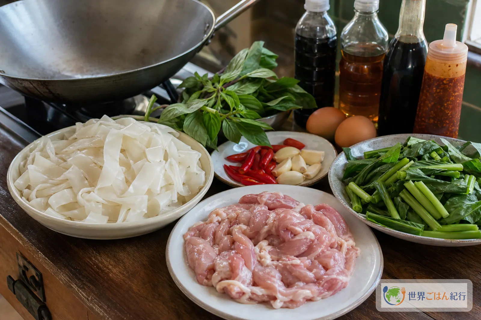 幅広米麺、鶏肉、カイラン、唐辛子、にんにく、バジル、卵、調味料を並べたパッキーマオの材料